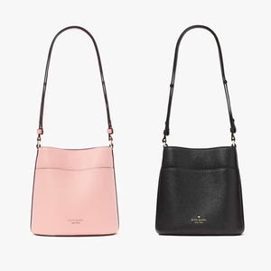 Two shoulder bags, one pale pink and one black, with smooth finishes and branded logos.