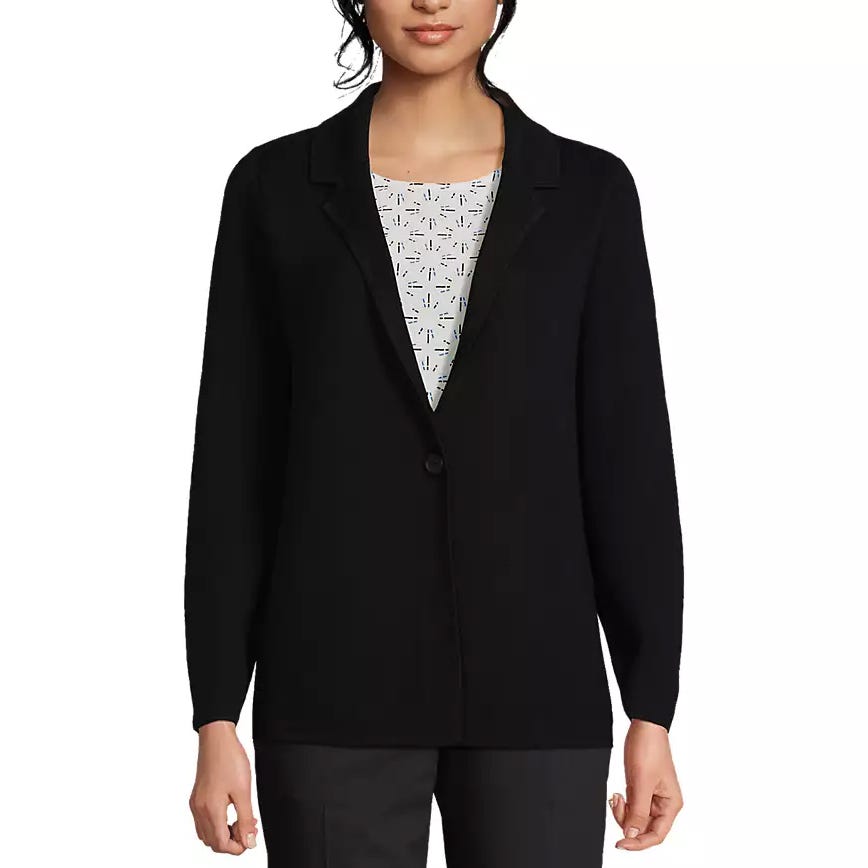 A woman is wearing a black blazer over a patterned top, paired with dark pants.