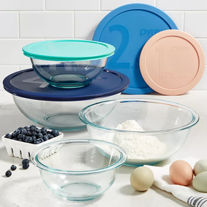 Set of glass mixing bowls with different colored plastic lids, ingredients like eggs, flour, and blueberries nearby.
