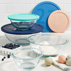 Set of glass mixing bowls with different colored plastic lids, ingredients like eggs, flour, and blueberries nearby.
