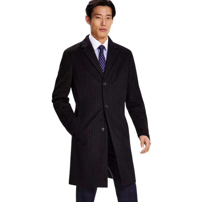 A man in a dark pinstripe coat, white shirt, and tie, paired with dark checkered trousers and black formal shoes.