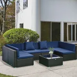 Outdoor patio furniture set featuring a navy-blue cushioned sectional sofa and a matching coffee table on a concrete patio, with a white building and greenery in the background.