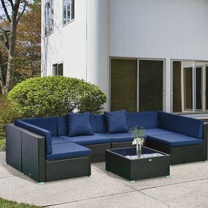 Outdoor patio furniture set featuring a navy-blue cushioned sectional sofa and a matching coffee table on a concrete patio, with a white building and greenery in the background.