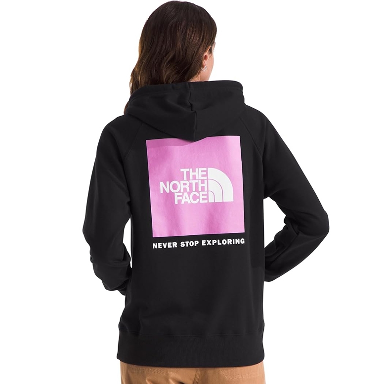 A person is wearing a black hoodie with a pink square featuring \“THE NORTH FACE\“ logo and the phrase \“NEVER STOP EXPLORING\“ printed on the back.
