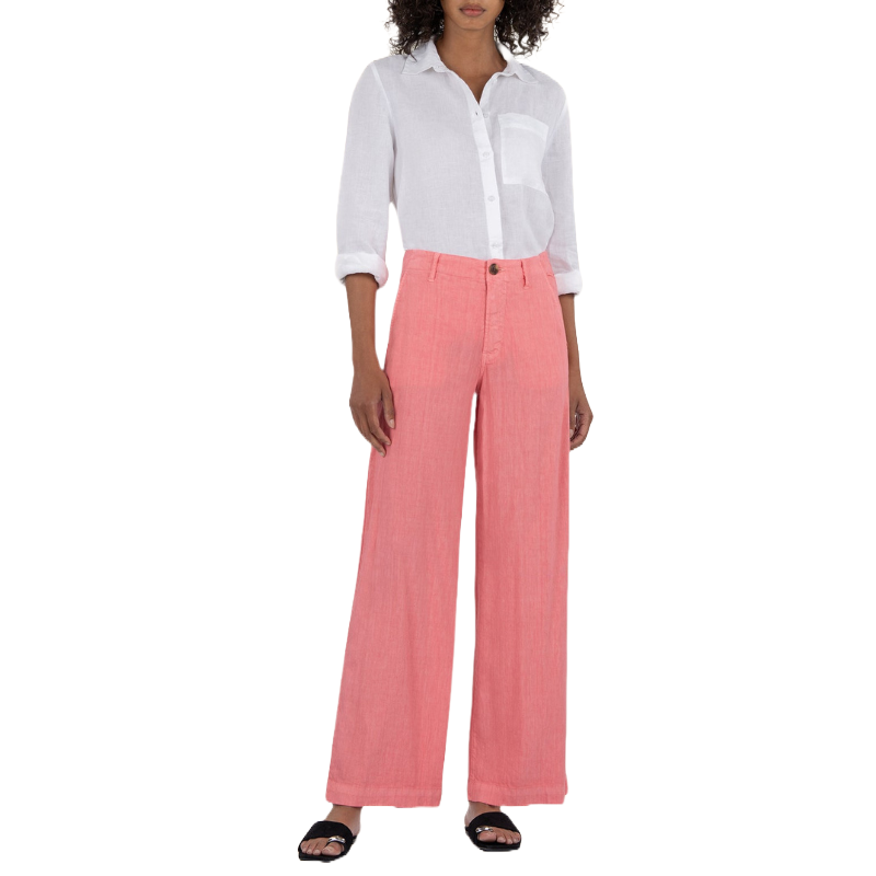 A woman is wearing a white button-up shirt with rolled sleeves and coral wide-leg pants, paired with black open-toe sandals.
