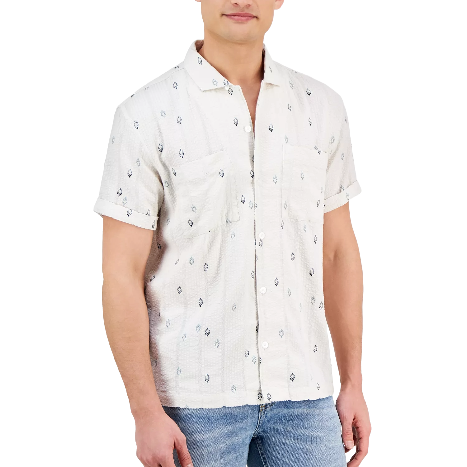 A man wears a short-sleeve white shirt with a subtle patterned design and two chest pockets, paired with light blue jeans.
