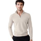 A man wearing a light beige half-zip sweater with long sleeves and black pants, standing against a light-colored background.