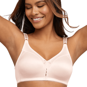 A woman is wearing a light pink, wireless, soft-cup bra with lace detail and adjustable straps. She is smiling with her arms raised.