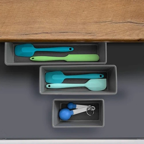 Three drawers containing silicone kitchen utensils in green and blue shades, and a measuring spoon set.