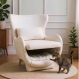 A cozy armchair with a hidden pet bed compartment is styled in a serene living room setting, accompanied by a playful tabby cat.