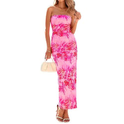 A woman is wearing a strapless, bodycon maxi dress with a pink and purple floral pattern, holding a small white handbag and wearing white strappy heels.