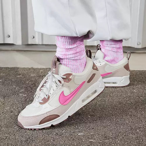 A pair of beige and pink sneakers with a prominent swoosh logo, paired with pink socks and white trousers.