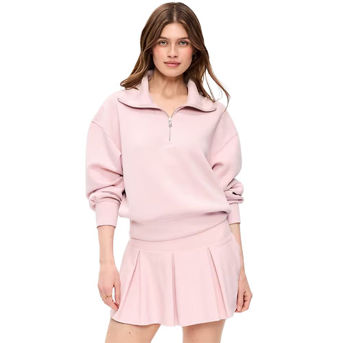 A woman wears a light pink long-sleeve sweatshirt with a quarter-zip collar paired with a matching pleated skirt.