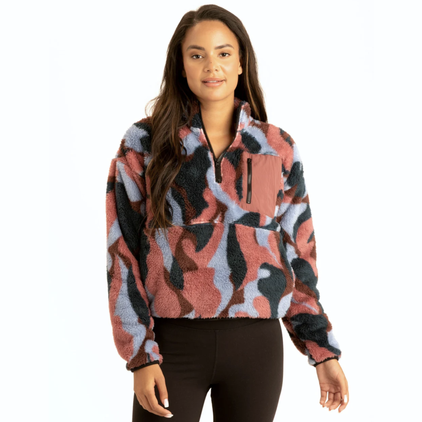 A woman is wearing a camouflage-patterned sherpa pullover with a zipper and a chest pocket, paired with black leggings.
