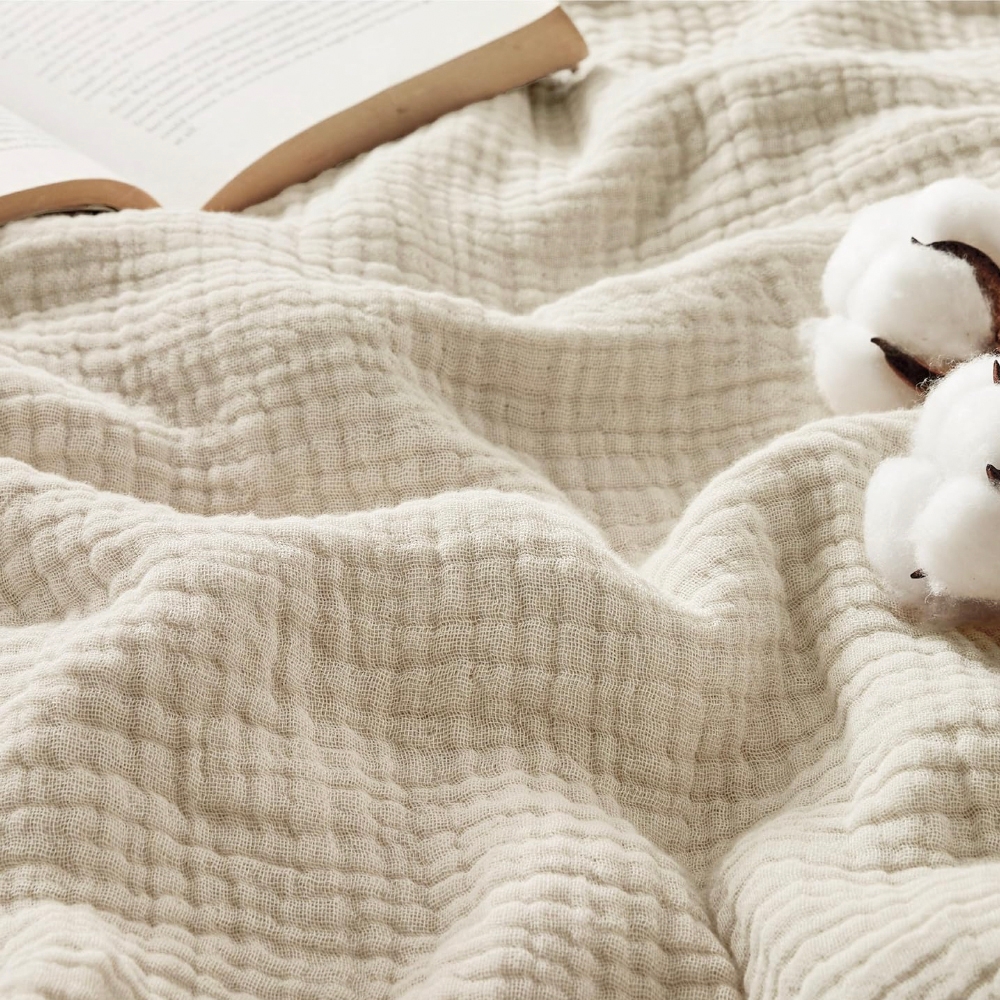 A textured cream-colored fabric is shown with an open book and cotton bolls placed on it.