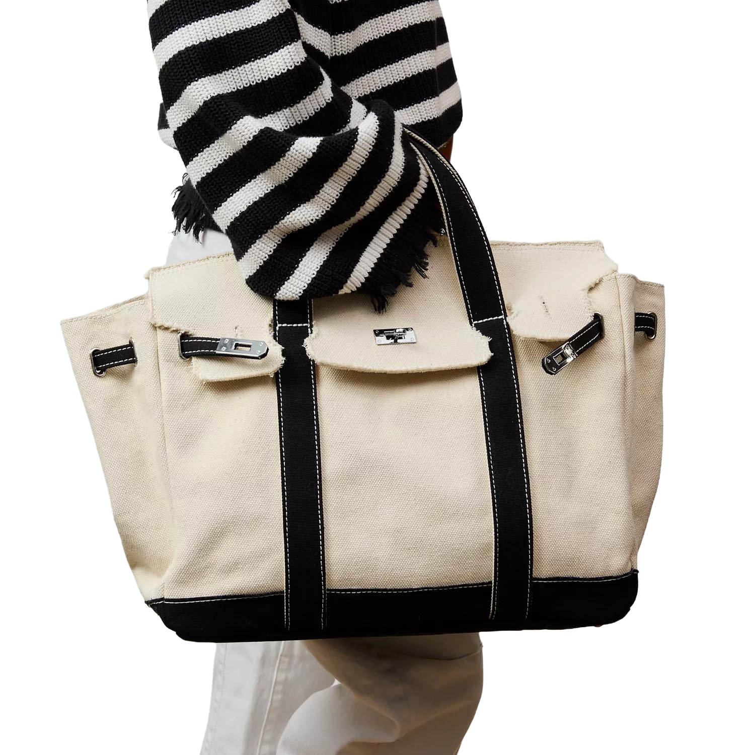 A person in a black and white striped sweater holds an off-white canvas tote bag with black trim and silver hardware.