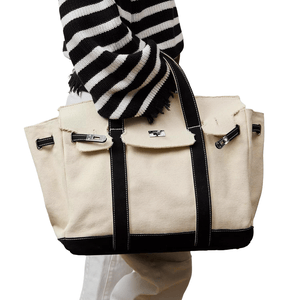 A person in a black and white striped sweater holds an off-white canvas tote bag with black trim and silver hardware.