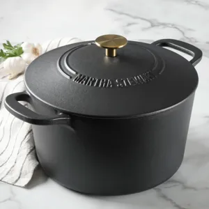 A black cast iron Dutch oven with a brass handle on the lid, featuring the name \“Martha Stewart\“ embossed on top.