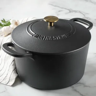 A black cast iron Dutch oven with a brass handle on the lid, featuring the name \“Martha Stewart\“ embossed on top.