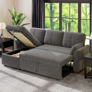 Gray upholstered sectional sofa with a pull-out bed feature and an open storage compartment, set in a room with large windows and indoor plants.