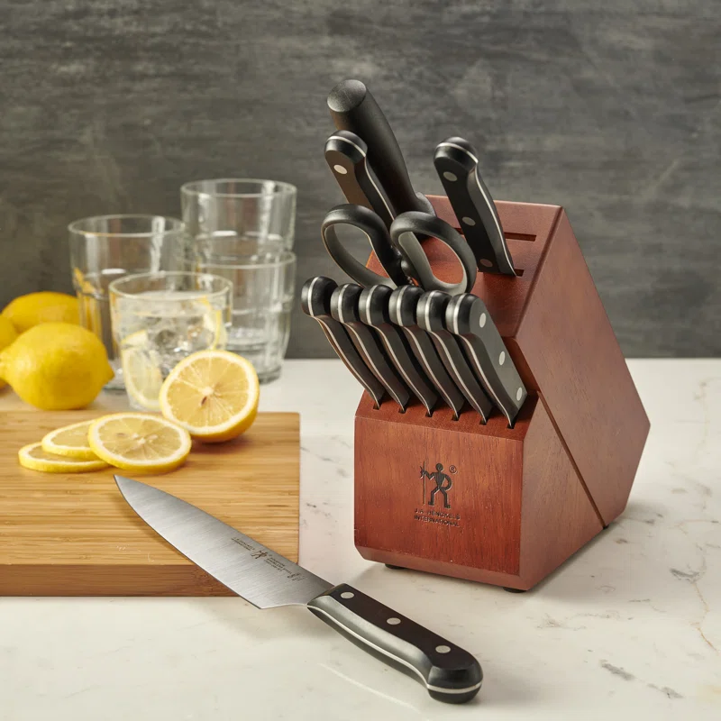 A set of kitchen knives in a wooden block with a chef's knife in front, alongside lemons and glasses on a marble countertop.