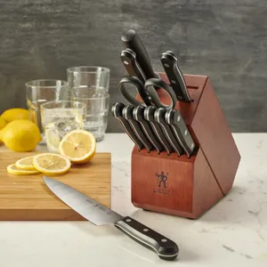 A set of kitchen knives in a wooden block with a chef's knife in front, alongside lemons and glasses on a marble countertop.