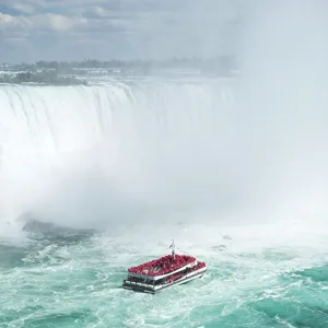 A tour boat filled with people in red ponchos approaches the misty base of Niagara Falls against a backdrop of powerful cascading water.