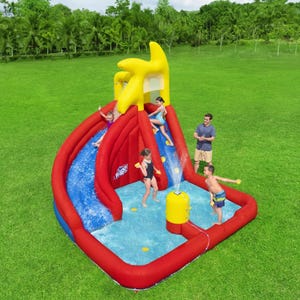 The H2Go Inflatable Mega Water Park features a vibrant red and yellow design with two water slides, a pool area, and a built-in sprinkler. Children are seen playing and sliding, supervised by an adult, set in a large grassy field.