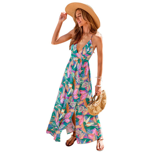 A woman is wearing a colorful, floral-patterned maxi dress with a deep neckline, paired with a straw hat, flat sandals, and holding a woven circular handbag.