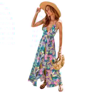 A woman is wearing a colorful, floral-patterned maxi dress with a deep neckline, paired with a straw hat, flat sandals, and holding a woven circular handbag.