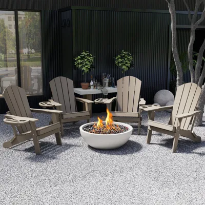A patio setup featuring four beige Adirondack chairs encircling a fire pit. There is a table with plants and bottled drinks in the background, set against a dark wall.