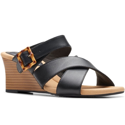 Black wedge sandal with wide leather straps and a brown tortoiseshell buckle. It features a tan footbed and stacked wedge heel.