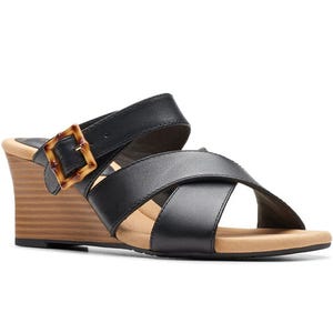 Black wedge sandal with wide leather straps and a brown tortoiseshell buckle. It features a tan footbed and stacked wedge heel.