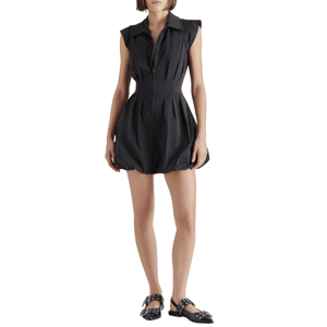 A woman wears a black sleeveless, collared dress with a zip front and a bubble hem, paired with black flats featuring metal buckle details.