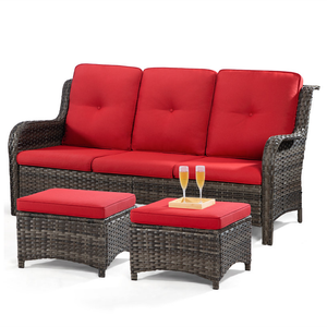 A three-seater all-weather wicker patio sofa with red cushions, accompanied by two matching ottomans. The ottomans feature trays with two glasses of sparkling liquid on top.