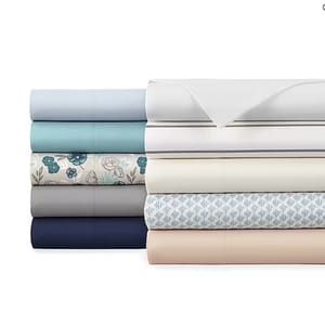 A stack of neatly folded bed sheets in various colors and patterns, including plain, floral, and geometric designs.