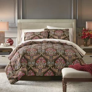 A bed is adorned with a floral-patterned comforter set, including matching pillows. The room features elegant decor with table lamps and a bench at the foot of the bed.