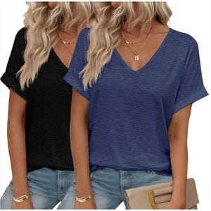 Two women wearing casual V-neck T-shirts, one in black and one in blue, paired with light blue jeans. They both have long blonde hair and are accessorized with gold necklaces and bracelets. One holds a beige clutch bag.