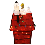 Christmas decoration featuring a lighted red doghouse with a plush white dog and a yellow bird on top, adorned with colorful string lights.