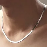 A simple silver necklace rests on a person's neck, featuring a smooth, flat chain design.