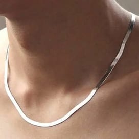 A simple silver necklace rests on a person's neck, featuring a smooth, flat chain design.