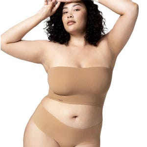 A woman is wearing a strapless bandeau bra and matching seamless underwear in a nude color.