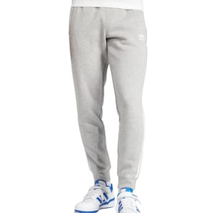 Gray Adidas Men's Adicolor Pants with a slim fit, featuring the Adidas logo on the upper thigh and white stripes along the sides. Paired with white sneakers with blue accents.