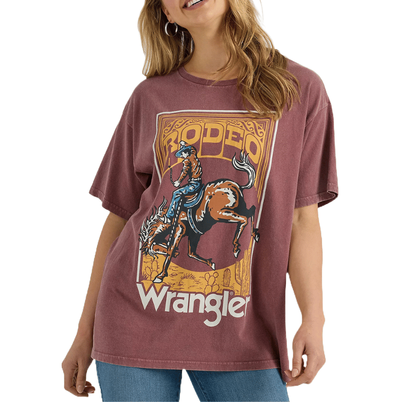 An oversized acid wash tee featuring a vintage-style rodeo graphic and \“Wrangler\“ logo, highlighting a cowboy riding a bucking bronco on a muted maroon background.