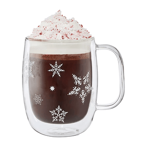 A glass holiday coffee mug featuring decorative snowflakes, filled with hot chocolate topped with whipped cream. The clear mug's design adds a festive touch, showcasing the drink's contents beautifully.