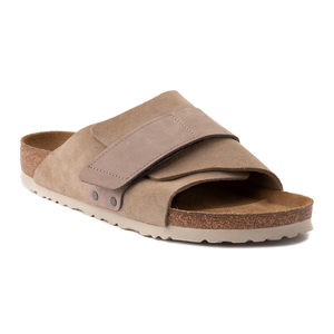 A pair of beige suede slide sandals with an adjustable strap and cork sole.