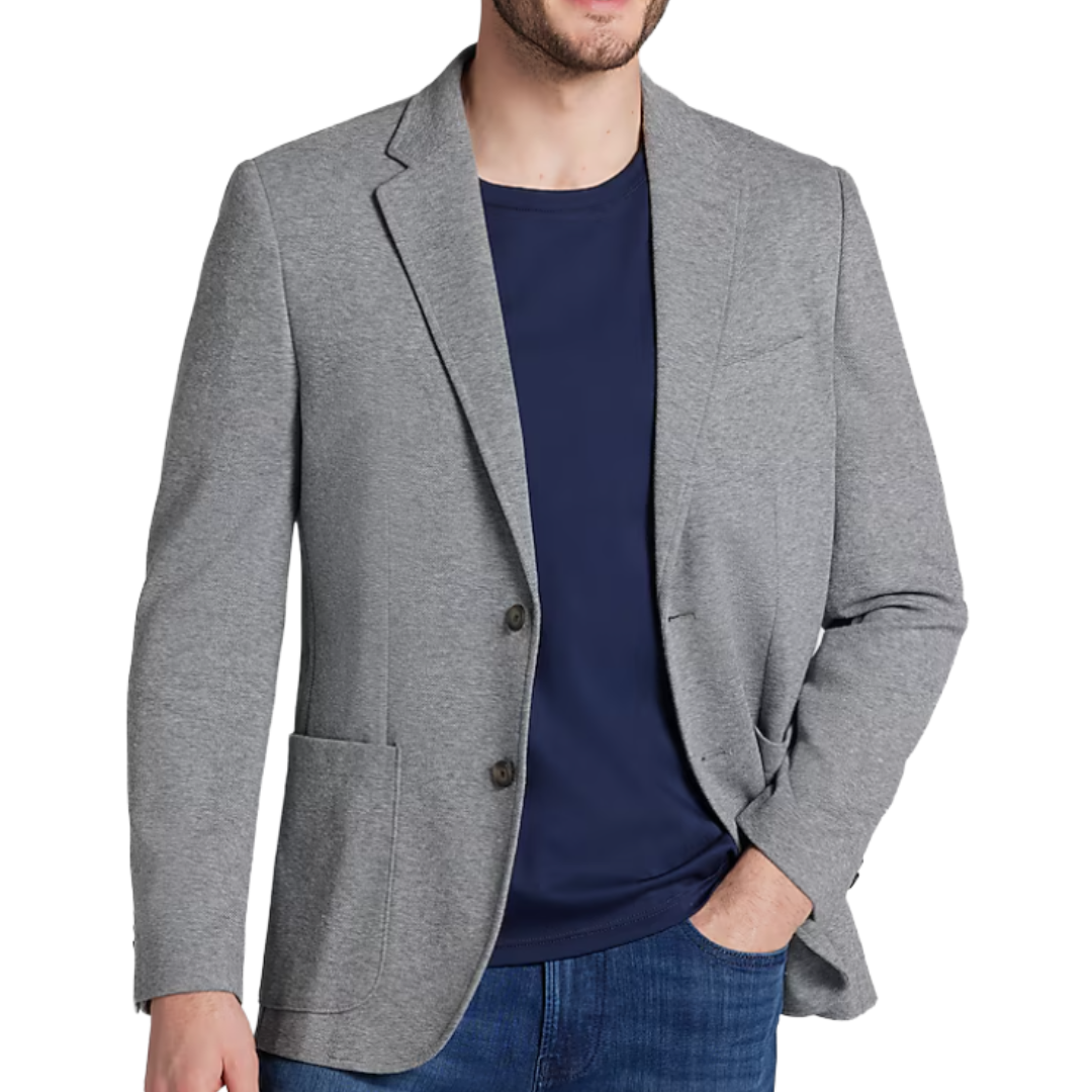 A man wearing a light gray blazer over a navy T-shirt, paired with blue jeans.