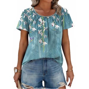 A teal Boho summer top with short sleeves features a floral print with cascading white blossoms and a relaxed fit, paired with distressed denim shorts.