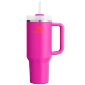 A pink travel mug with a handle and straw, featuring the brand Stanley on its side.