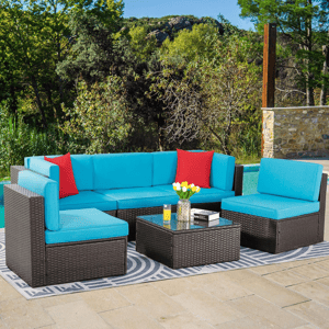 Outdoor sectional set with blue cushions and red pillows, featuring a glass-top coffee table, situated on a geometric outdoor rug by a pool.